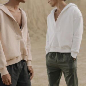 Two models wearing minimalist hoodies in a neutral outdoor setting. Modern fashion style captured.